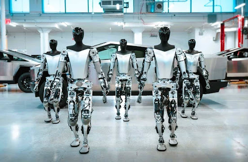 A row of Tesla Optimus humanoid robots standing in a factory